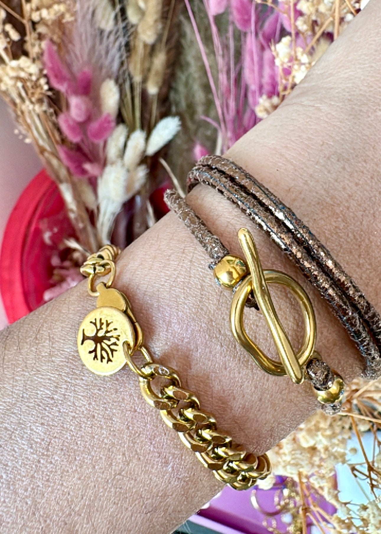 Gold bracelets on a wrist with dried flowers in the background
