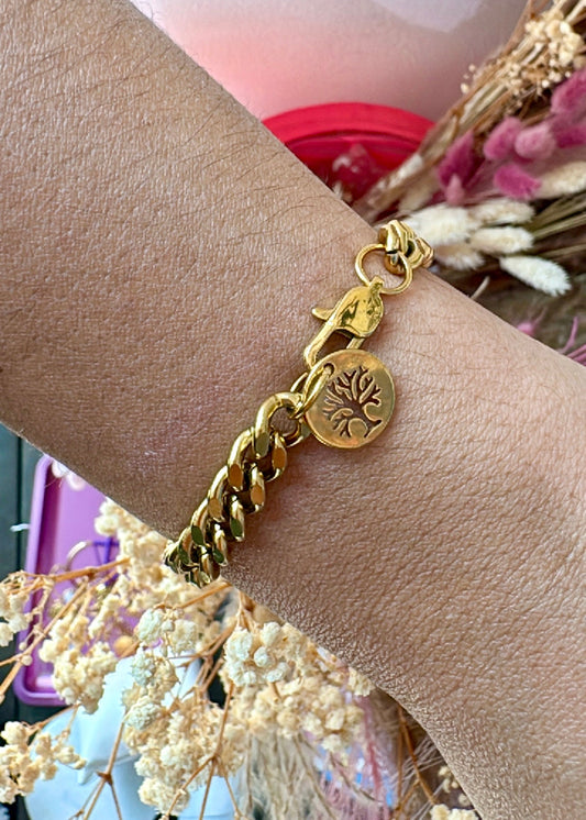 Gold bracelet with tree of life charm on a wrist, blurred background