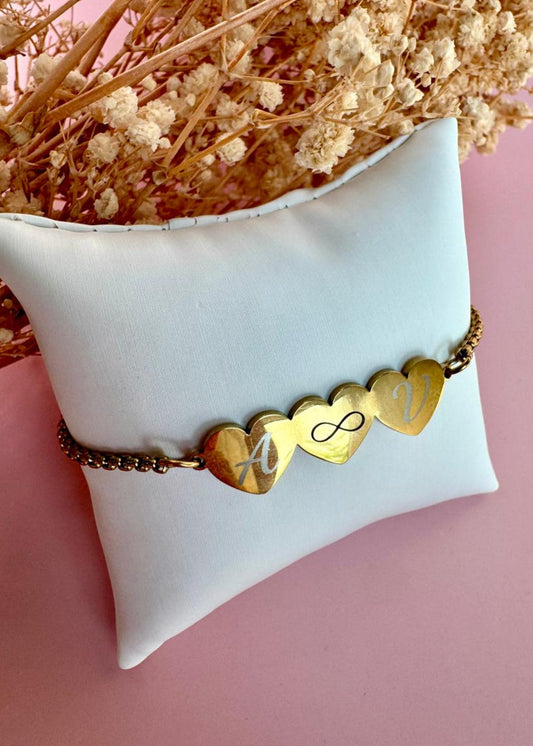 Gold bracelet with heart-shaped charms on a white pillow with dried flowers in the background