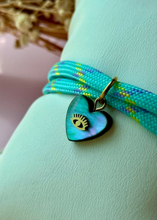Turquoise braided bracelet with a heart-shaped pendant featuring an eye design on a light green surface.